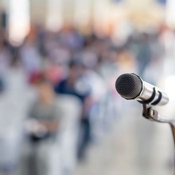 Symbolbild: Versammlung Redner-Mikrofon vor verschwommenem Auditorium